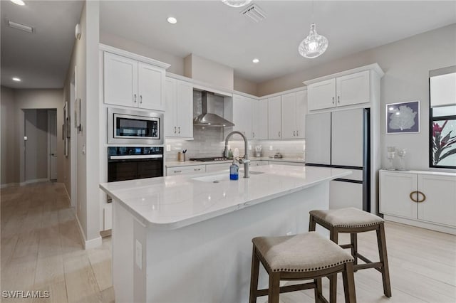 kitchen with decorative backsplash, appliances with stainless steel finishes, light wood-style floors, white cabinetry, and wall chimney exhaust hood