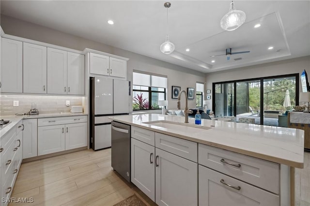 kitchen featuring dishwasher, freestanding refrigerator, a tray ceiling, white cabinetry, and a sink