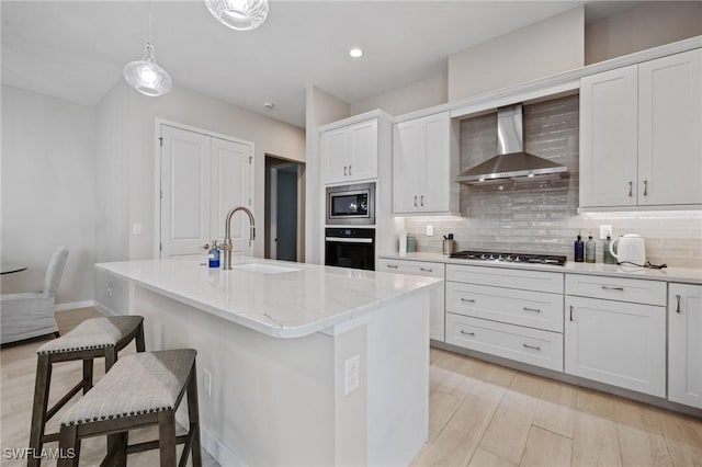 kitchen featuring wall chimney exhaust hood, tasteful backsplash, appliances with stainless steel finishes, a sink, and a kitchen bar