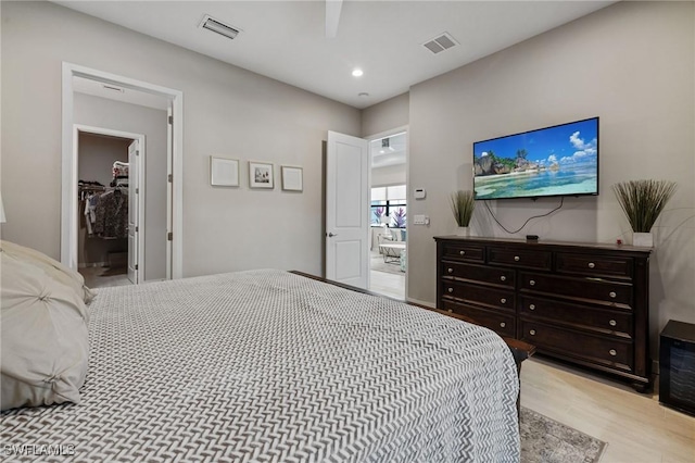 bedroom featuring light wood-style flooring, a walk in closet, visible vents, and recessed lighting