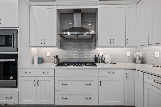 kitchen featuring stainless steel appliances, white cabinets, wall chimney exhaust hood, and tasteful backsplash