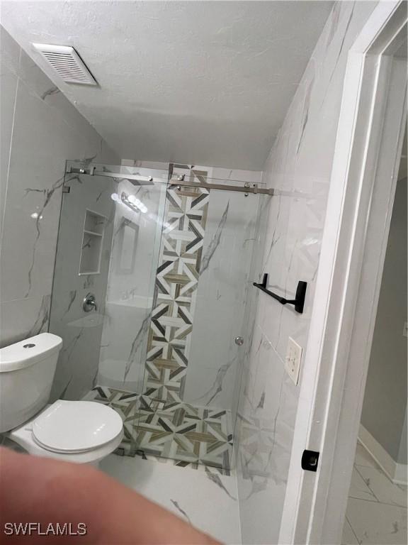 bathroom with a marble finish shower, visible vents, and marble finish floor