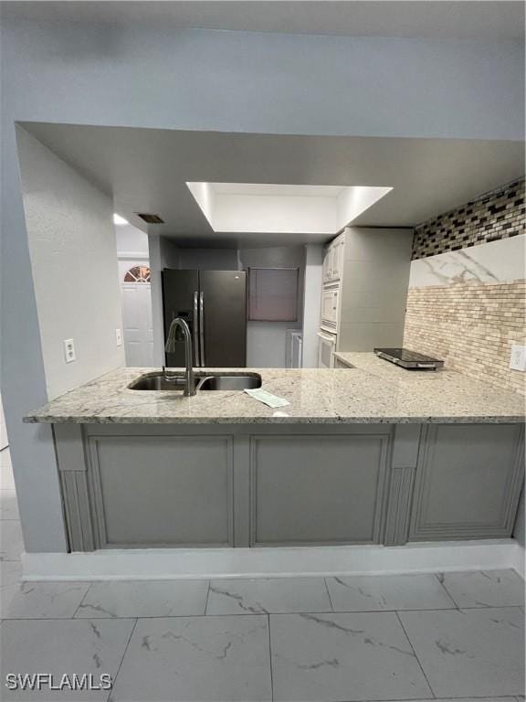 kitchen featuring light stone countertops, a peninsula, a sink, refrigerator with ice dispenser, and marble finish floor