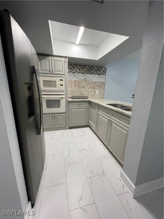 kitchen featuring marble finish floor, gray cabinetry, backsplash, white appliances, and light countertops