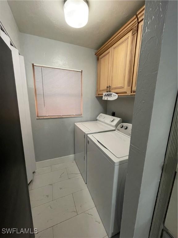 clothes washing area with cabinet space, independent washer and dryer, marble finish floor, and baseboards