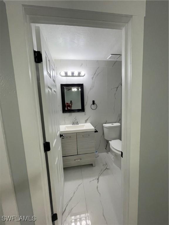 bathroom with vanity, toilet, and marble finish floor