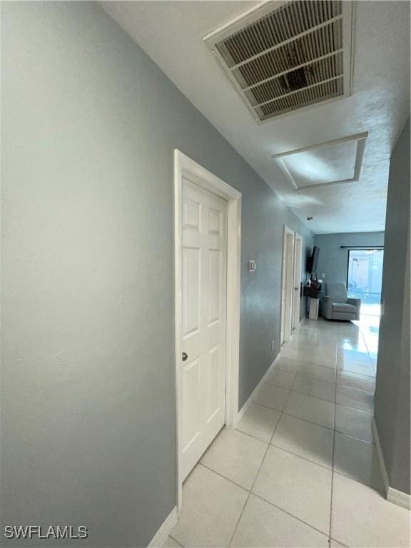 corridor featuring light tile patterned flooring, visible vents, attic access, and baseboards