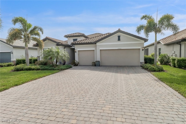 view of front of house featuring a front lawn, a tile roof, stucco siding, decorative driveway, and an attached garage