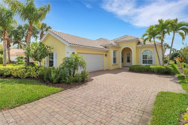 mediterranean / spanish-style house featuring a garage, a tiled roof, decorative driveway, and stucco siding