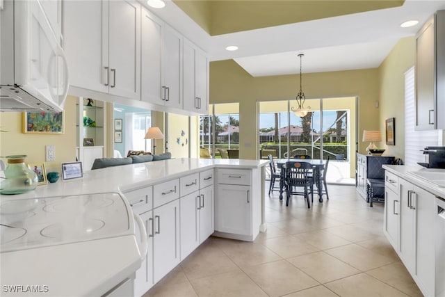 kitchen featuring pendant lighting, white microwave, white cabinetry, range, and a peninsula