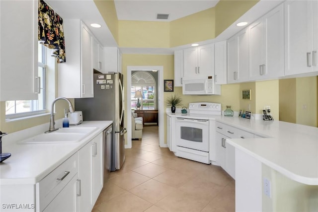 kitchen with a peninsula, white appliances, a sink, visible vents, and white cabinetry