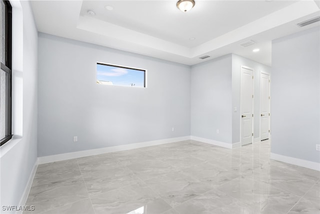 spare room with visible vents, a tray ceiling, and baseboards