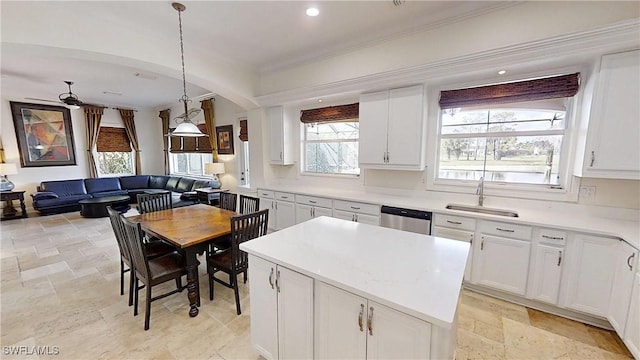 kitchen with a kitchen island, a sink, white cabinets, stone finish flooring, and stainless steel dishwasher