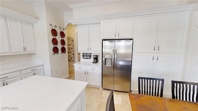 kitchen featuring arched walkways, stainless steel fridge, white cabinetry, and ornamental molding