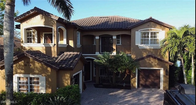 mediterranean / spanish-style house featuring a tiled roof, decorative driveway, a garage, and stucco siding