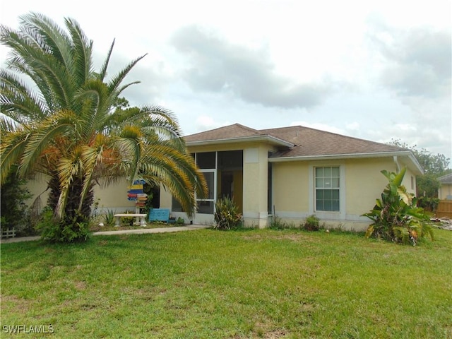 back of house featuring a sunroom, a lawn, and stucco siding