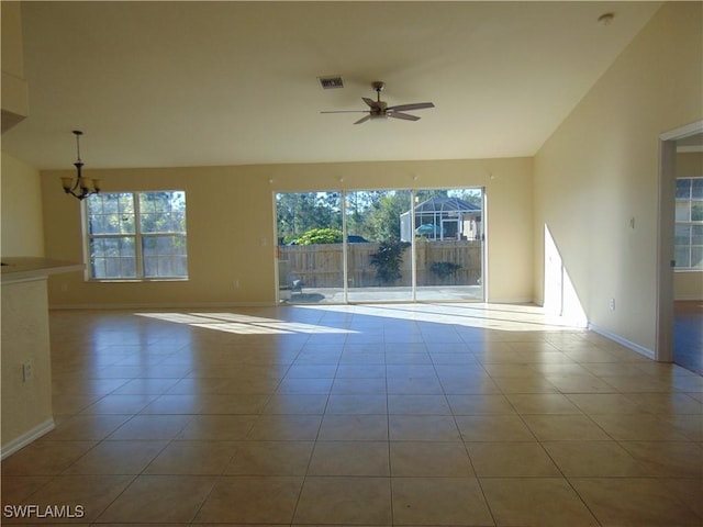 tiled spare room featuring visible vents, vaulted ceiling, baseboards, and ceiling fan with notable chandelier