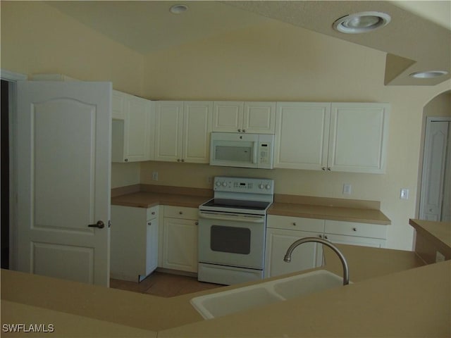 kitchen featuring lofted ceiling, light tile patterned floors, white appliances, a sink, and white cabinets