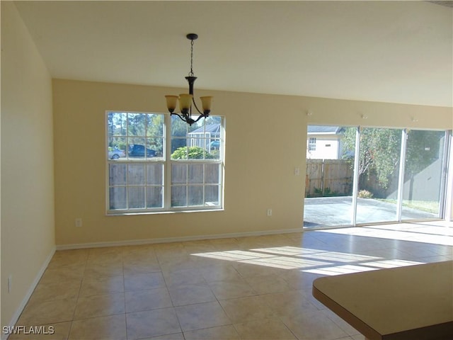 tiled empty room with baseboards, plenty of natural light, and an inviting chandelier