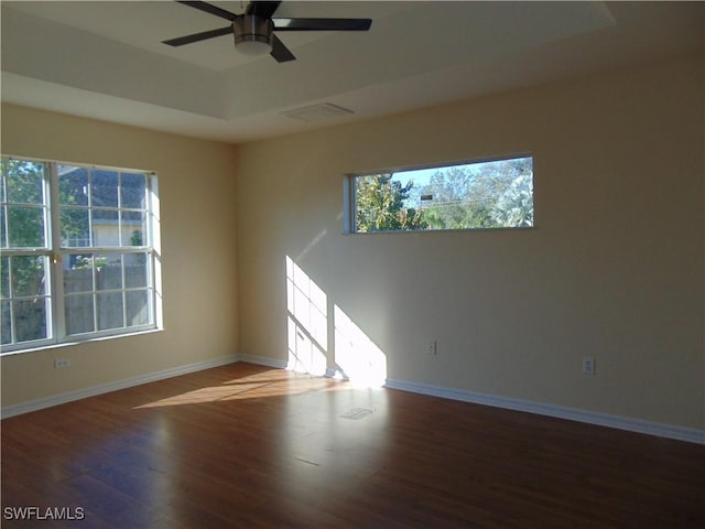 spare room featuring a raised ceiling, baseboards, and wood finished floors