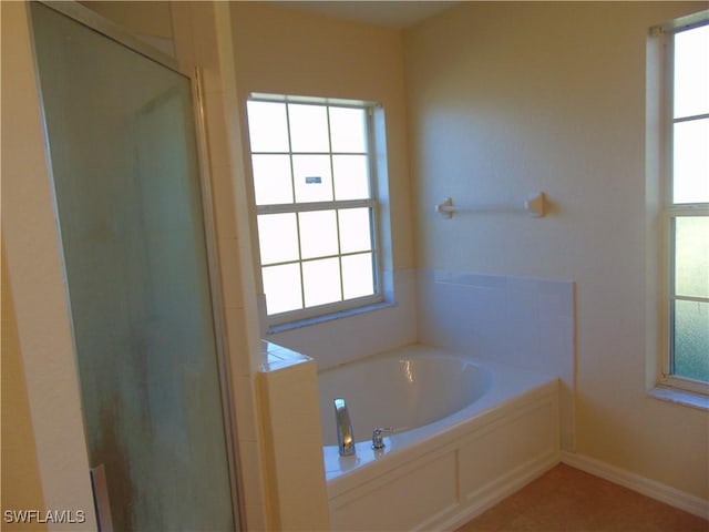 full bath featuring a stall shower, a garden tub, and baseboards