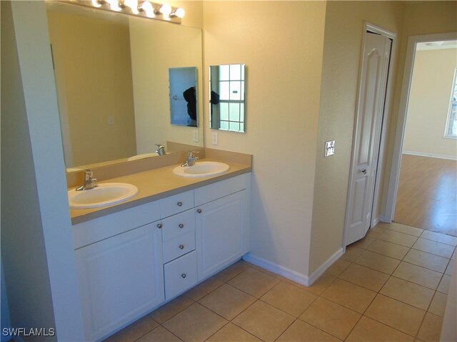 full bath with baseboards, double vanity, a sink, and tile patterned floors