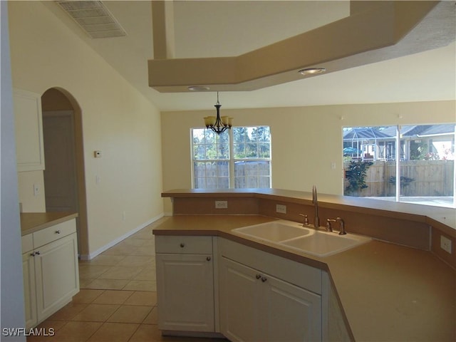 kitchen featuring arched walkways, light tile patterned floors, visible vents, white cabinets, and a sink