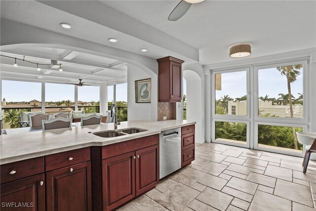 kitchen featuring a ceiling fan, light stone countertops, dark brown cabinets, stainless steel dishwasher, and a sink