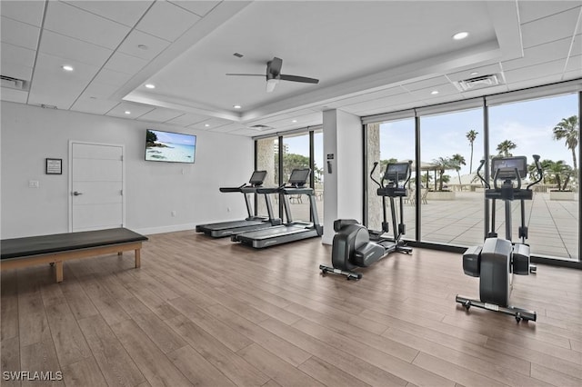 workout area with a raised ceiling, visible vents, wood finished floors, a wall of windows, and baseboards