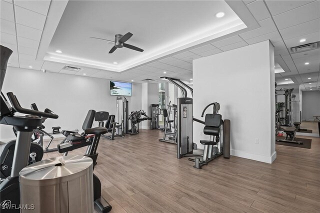 gym with a raised ceiling, visible vents, ceiling fan, and wood finished floors