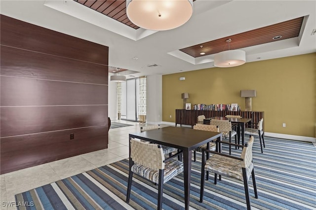 dining room featuring a tray ceiling, baseboards, and tile patterned floors