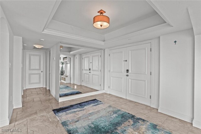 entrance foyer with a tray ceiling, stone finish flooring, and baseboards