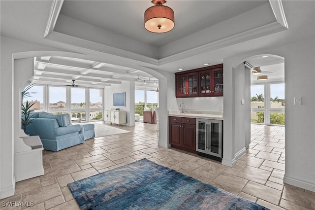 bar featuring arched walkways, beverage cooler, a tray ceiling, and ceiling fan