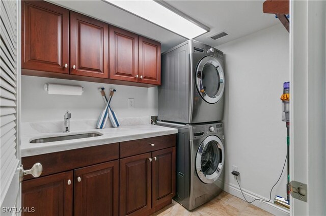 laundry room featuring stacked washer and dryer, a sink, visible vents, baseboards, and cabinet space