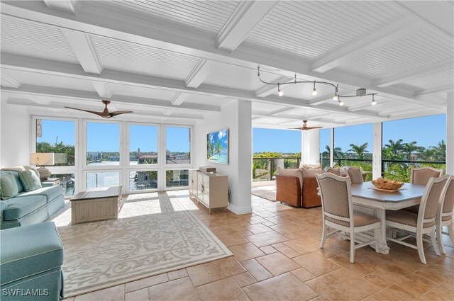 sunroom featuring baseboards, beam ceiling, stone tile flooring, and a healthy amount of sunlight