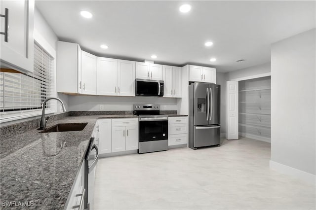 kitchen featuring dark stone countertops, white cabinetry, stainless steel appliances, and a sink