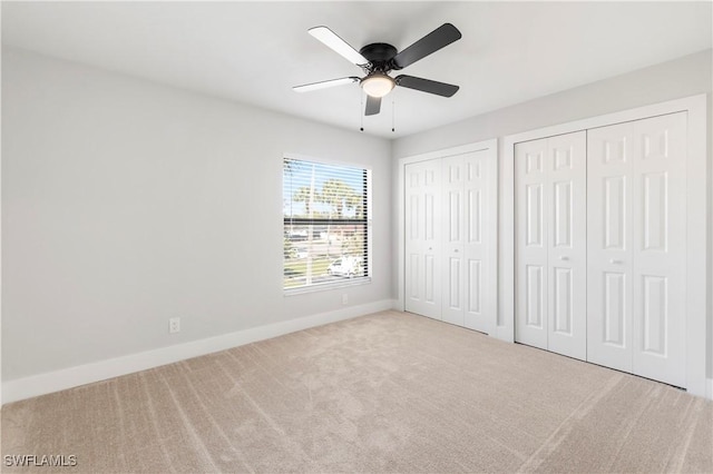 unfurnished bedroom featuring baseboards, multiple closets, a ceiling fan, and carpet flooring