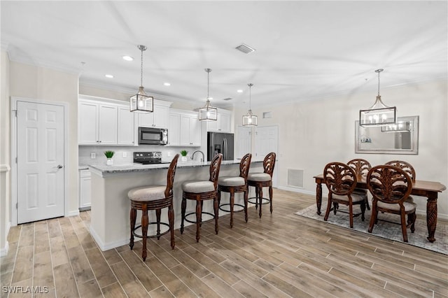 kitchen with visible vents, a center island with sink, white cabinetry, and stainless steel appliances