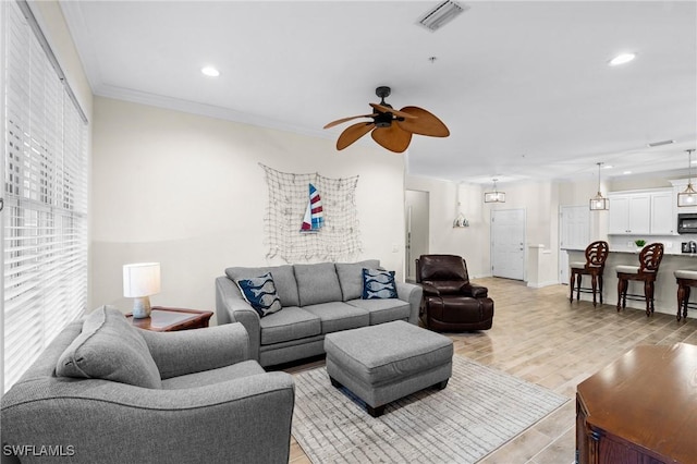 living room featuring light wood-type flooring, visible vents, a healthy amount of sunlight, and crown molding