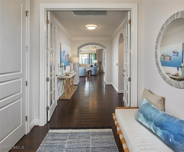 hallway with arched walkways, visible vents, crown molding, and wood finished floors