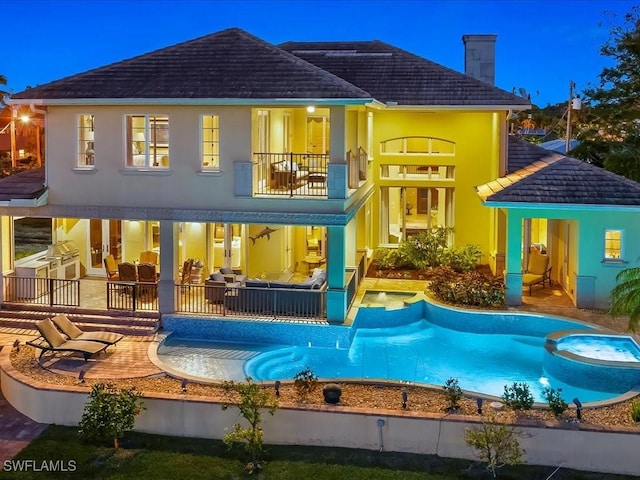 rear view of property featuring a pool with connected hot tub, stucco siding, a chimney, a balcony, and a patio area