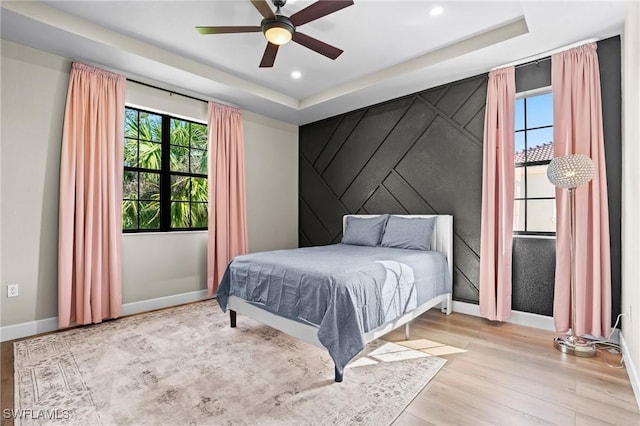 bedroom featuring an accent wall, multiple windows, wood finished floors, and baseboards