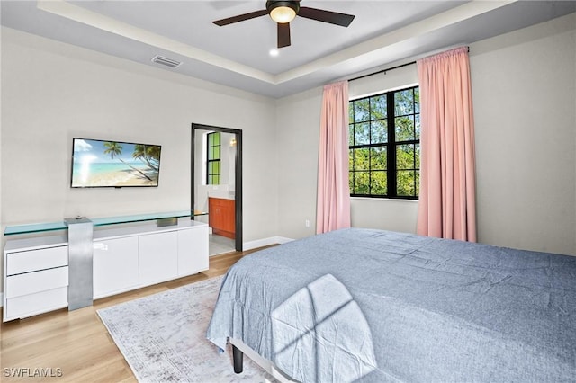 bedroom with baseboards, visible vents, ceiling fan, a raised ceiling, and light wood-type flooring