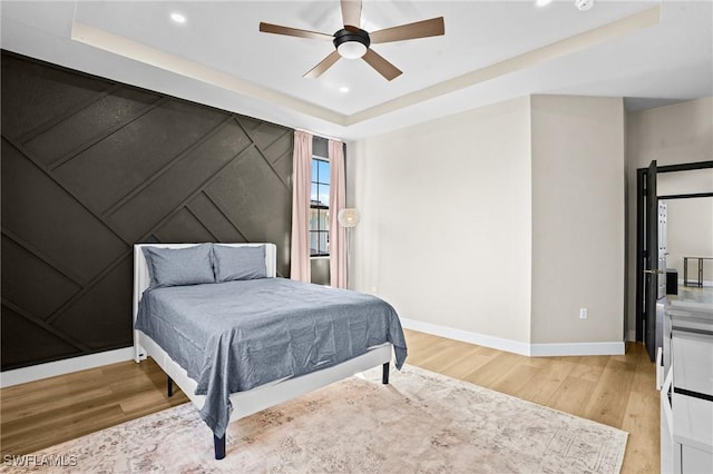 bedroom featuring baseboards, a tray ceiling, recessed lighting, light wood-style flooring, and a ceiling fan