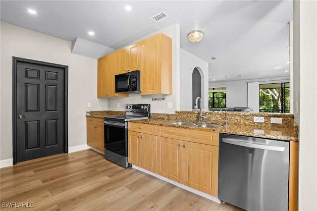 kitchen with light brown cabinetry, dark stone countertops, stainless steel appliances, and a sink