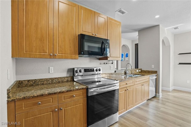 kitchen with visible vents, light wood-style flooring, a sink, dark stone countertops, and appliances with stainless steel finishes