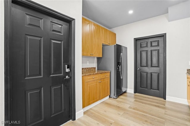 kitchen featuring light wood-type flooring, light stone counters, brown cabinetry, stainless steel fridge with ice dispenser, and baseboards