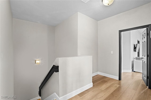 hallway with baseboards, an upstairs landing, and light wood-style flooring