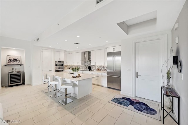 kitchen with a breakfast bar area, white cabinets, appliances with stainless steel finishes, backsplash, and wall chimney exhaust hood