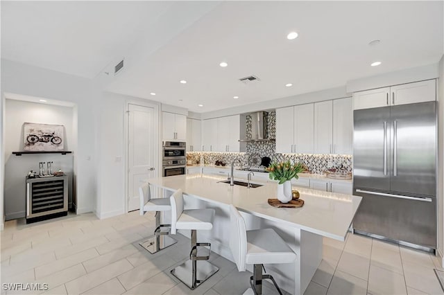 kitchen with a sink, visible vents, light countertops, appliances with stainless steel finishes, and wall chimney exhaust hood